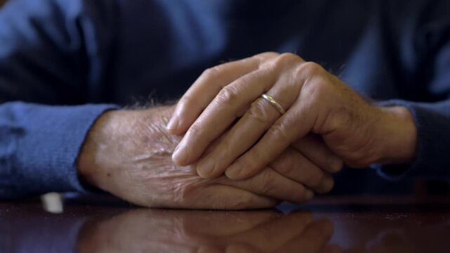 ands of a mature man massage each other slowly while dealing with chronic body pain, joint discomfort and physical suffering inside a home environment.