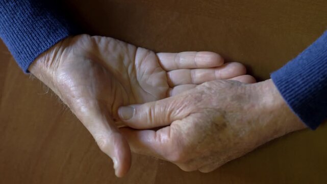 Overhead view of elderly man hands massaging each other slowly while coping with chronic joint pain and physical discomfort inside a home environment.