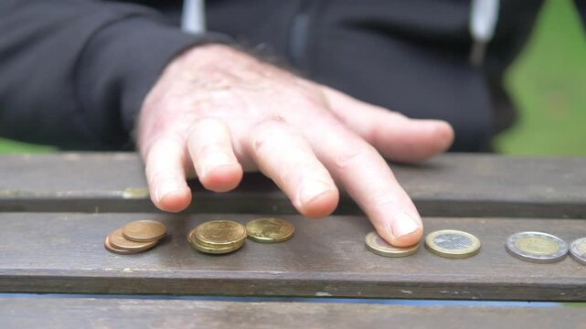 Mature man hands counting a few remaining coins on a garden table, highlighting financial concern and economic hardship.