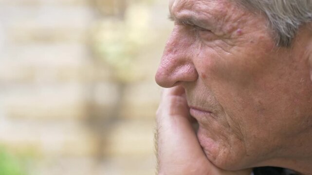 Side profile of a mature white-haired man outdoors looking overwhelmed by problems, with a worried expression that conveys stress, concern and emotional burden.