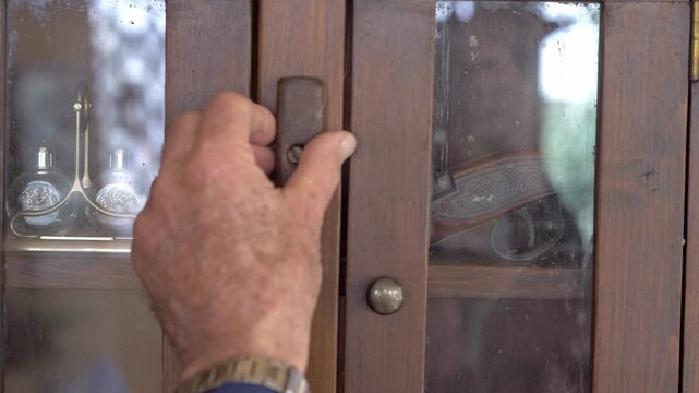 Close-up of mature male hands opening a small wooden cabinet and removing an antique pistol, suggesting secrecy, history and hidden danger.