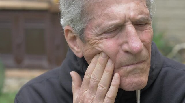 Attractive mature man with gray hair touches his cheek while suffering from a painful toothache at home, expressing physical discomfort and dental pain indoors