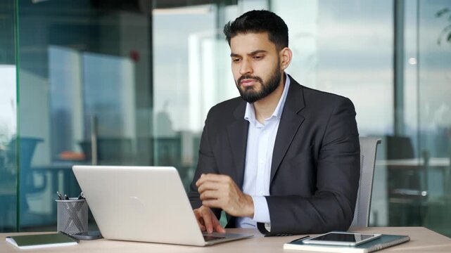 Thoughtful businessman thinking about problem solving while working on laptop sitting at workplace in business office. Focused serious manager in a formal suit is busy with startup project on computer