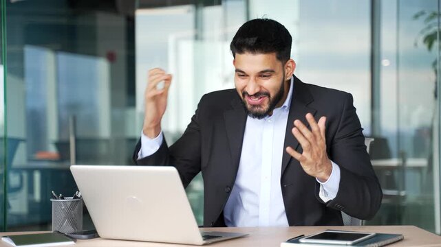 Happy excited businessman received great news on laptop sitting at workplace in business office. Smiling shocked surprised worker celebrating success after reading a positive good message on computer