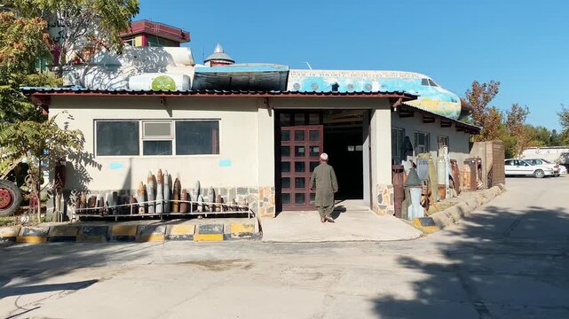 Kabul, Afghanistan - 25th october, 2024: OMAR Mine Museum Kabul exterior. Afghan man walking into a museum building decorated with an airplane fuselage and rows of deactivated unexploded bombs
