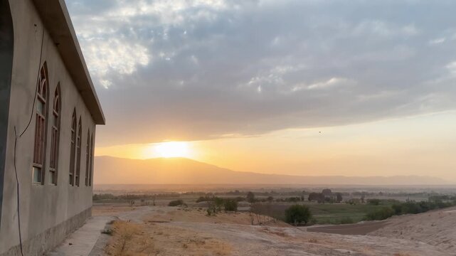 Afghan village mosque sunset. A simple concrete mosque with arched windows overlooks a vast, golden valley and the Hindu Kush mountains at dusk. Spiritual serenity in rural Afghanistan.