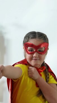 A girl wears a red mask and red cape, posing confidently. The girl seems ready for an adventure, showcasing her strong spirit with a playful fist.