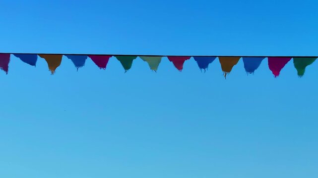 brightly colored triangular pennant flags on string gently fluttering in wind against beautiful, clear blue sky, creating festive, celebratory, and joyful atmosphere for summer event.