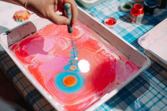 A man creates colorful ebru patterns on the water during a master class