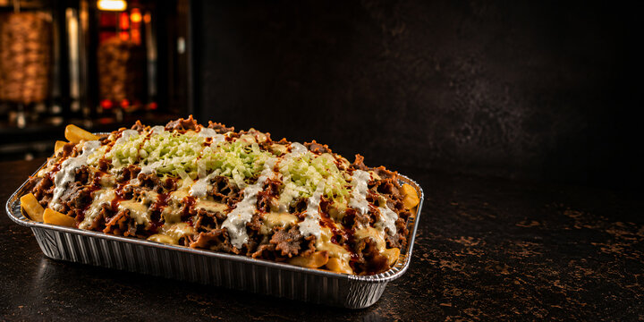 Cinematic Dutch kapsalon kebab fries in aluminum tray on dark studio table