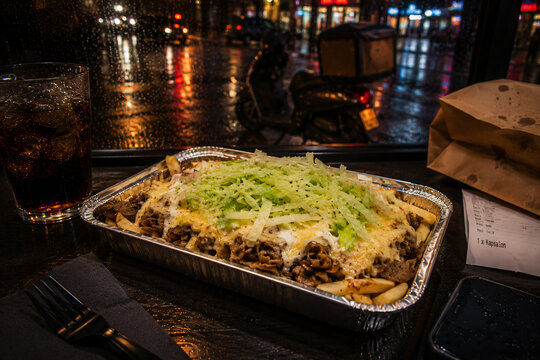 Dutch kapsalon takeaway meal in rainy urban delivery night scene