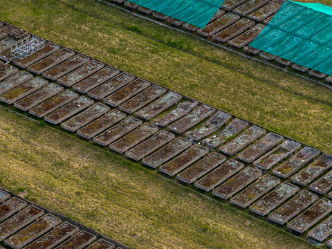 Aerial view of rows of rectangular concrete cultivation beds on a grassy field with green mesh covers in Vilnius County, Lithuania.
