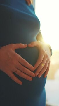A woman cradles her pregnant belly with both hands, showing a gentle connection. The woman wears a blue garment, highlighting the pregnancy and her hands.