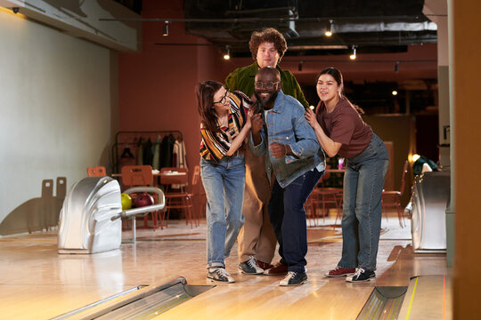 Wide shot of diverse young adults gathering at bowling lane, cheering and posing during team game. Representing friendship, leisure marketing, group activities, social campaign use