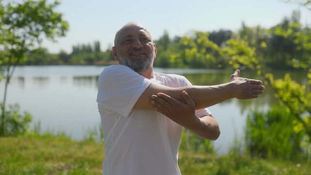 Senior man doing fitness arm stretches near lake outdoor workout session