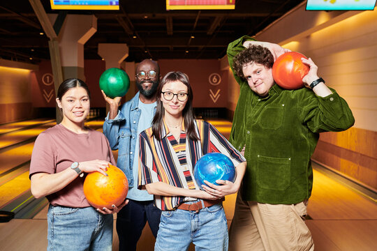 Portrait of diverse young adults holding bowling balls and posing in bowling alley, showing team bonding and leisure activity. Useful for workplace culture, friendship, group events marketing