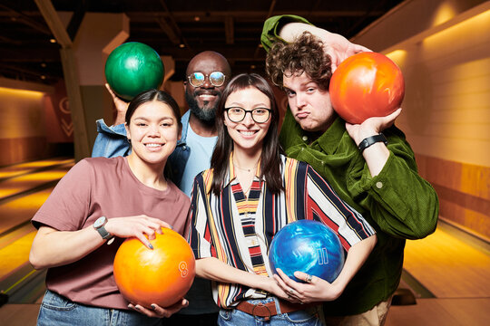 Portrait of diverse young adults holding bowling balls and posing in bowling alley, showing team leisure and friendship. Ideal for social events, group activities, recreation marketing