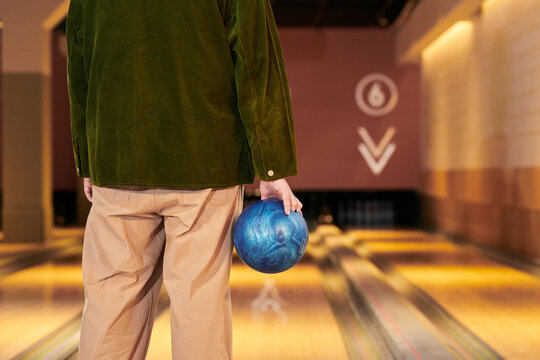 Rear view of young adult man holding bowling ball and preparing throw on lane, representing leisure activity and recreation. Ideal for entertainment marketing, social outing promotion