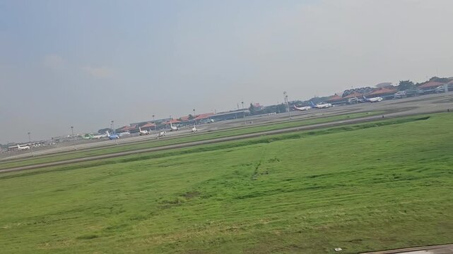 An expansive aerial view captures a commercial aircraft taking off from Soekarno-Hatta International Airport, revealing the massive GMF AeroAsia maintenance hangars, taxiways, and parked airplanes.