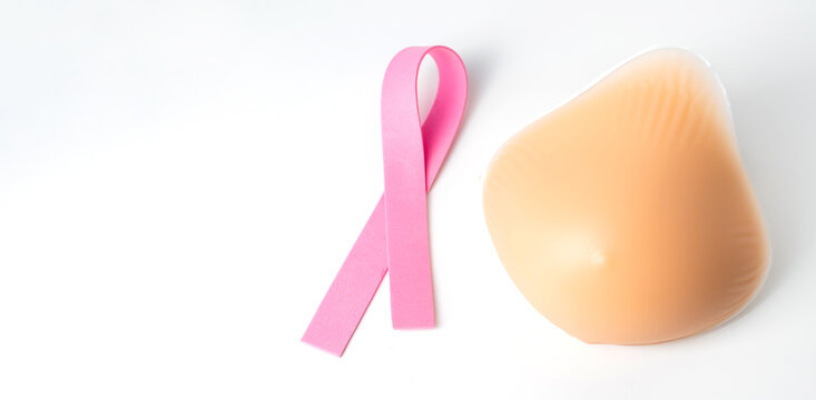 Pink ribbon symbolizing breast cancer awareness placed next to a silicone breast prosthesis on a white background, signifying post mastectomy recovery and support
