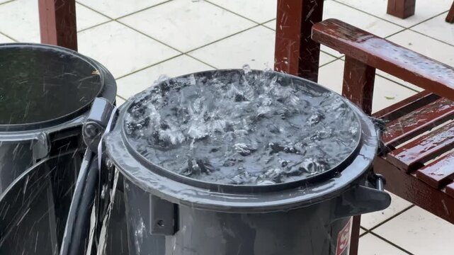 Es regnet in Str&ouml;men und das Wasser f&auml;llt vom Dach in eine Tonne