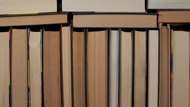 Collection of hardcover publications arranged closely on bookshelf surface, educational background featuring stacked printed volumes indoors