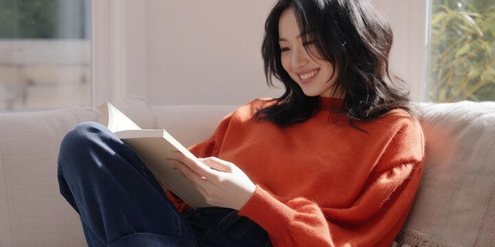 Young woman reading book on sofa near window in living room