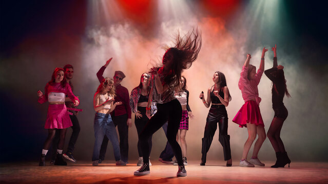 Female dancer with flying hair leading energetic group on smoky nightclub stage. Concept of dance party promo, club poster, music event campaign and bold youth nightlife advertising.