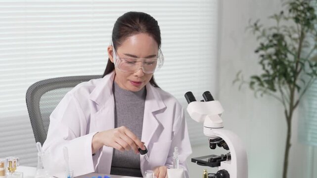 A female scientist is examining cosmetic samples under a microscope in a laboratory. The scientists are studying microplastics in the cosmetic ingredients.