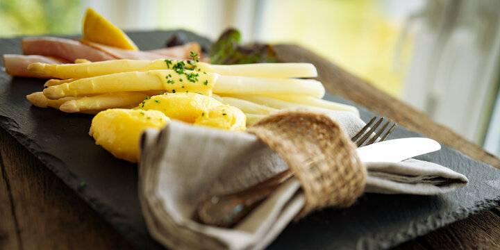 Seasonal white asparagus with creamy hollandaise sauce, served on a slate plate. Decoration suggestion for a modern seasonal cuisine. Close-up with short depth of field.