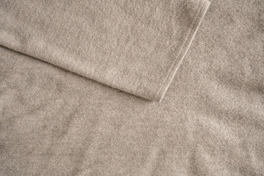 Natural texture of a beige wool fabric. Soft woven cotton texture featuring a draped sleeve from a sweater. Close-up. Top view.