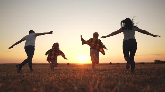 Family running in a field at sunset. Family, silhouette, running, park running together, sunset. Family running lifestyle together at sunset.