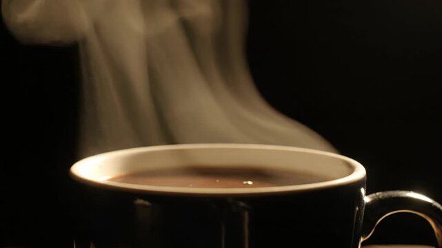 Cangkir Kopi Panas Hitam. Foto close-up menampilkan secangkir kopi hitam panas dalam cangkir berwarna gelap dengan uap tebal yang naik di latar belakang hitam, memberikan kesan hangat, elegan, dan coc