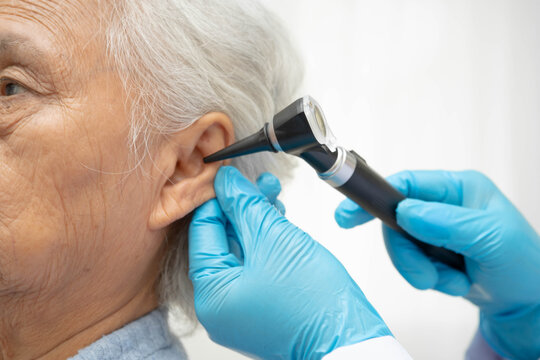 Otolaryngologist or ENT physician doctor examining senior patient ear with otoscope, hearing loss problem.