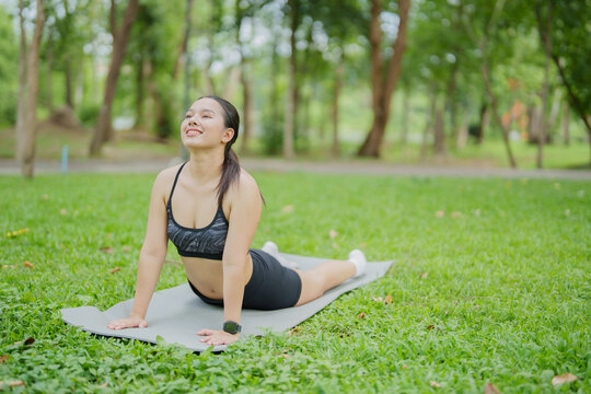 Young Asian woman performing a cobra yoga pose on a mat in a park, focusing on her upper body and back flexibility while enjoying an outdoor exercise for personal well-being