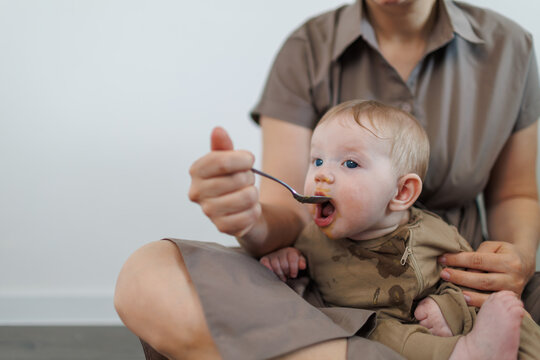 Close-up of a baby boy being spoon-fed by a woman in a domestic setting