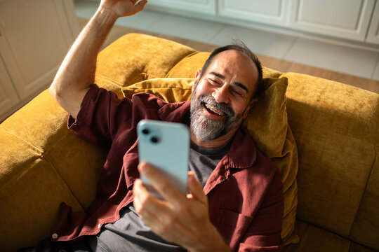 Cheerful mature man video chatting on sofa at home