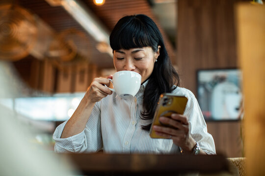 Woman drinking coffee and using smartphone at cafe