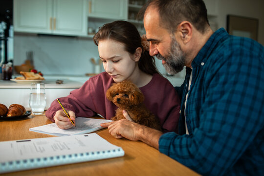 Father helping daughter with homework at kitchen table with puppy