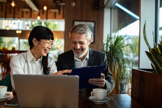 Two colleagues reviewing documents with laptop in a modern cafe