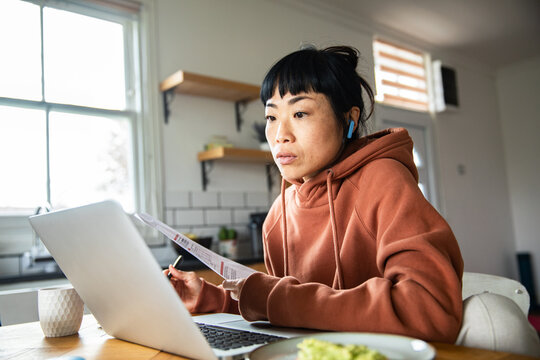 Focused woman paying bills on laptop at home kitchen table
