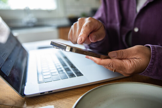 Person using smartphone and laptop at home workspace