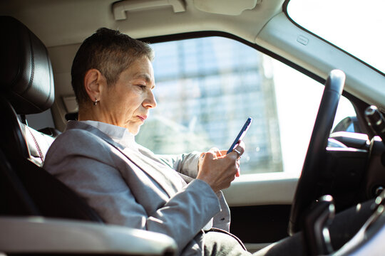 Senior businesswoman using smartphone in car during urban commute