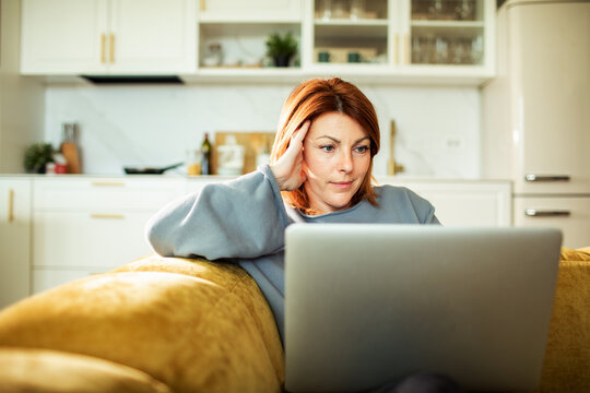 Focused woman using laptop on sofa in home kitchen