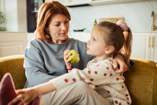Mother and daughter talking with apple on sofa at home