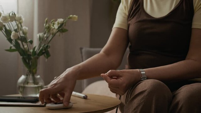 Cropped close up shot of senior woman performing fingerstick blood test then measuring glucose level with glucometer during daily diabetes treatment routine at home