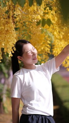 Fototapeta premium Young girl under yellow flower, Person standing under blooming yellow flower tree outdoors in spring