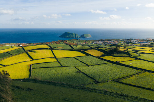Aerial view of the patchwork fields near Pico Dona Joana divided by stone walls overlooking the ocean and coastal village, Feteira, Acores, Portugal.