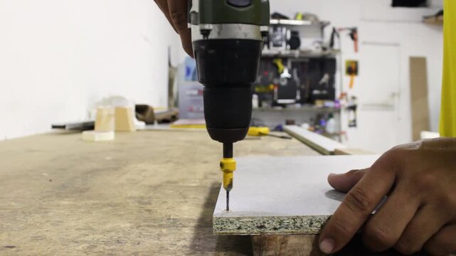 The hands of an unrecognizable worker are using an electric drill on a wooden board inside an upholstery workshop in Neiva, Huila, Colombia. Concept of industrial entrepreneurship