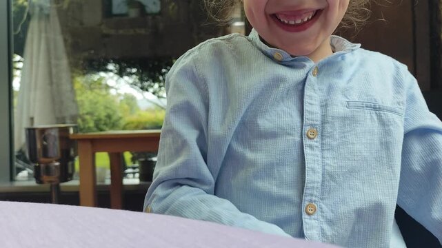 A cheerful young boy wearing a blue shirt smiles broadly and leans in towards the camera, proudly displaying his teeth and the gap from a missing tooth.